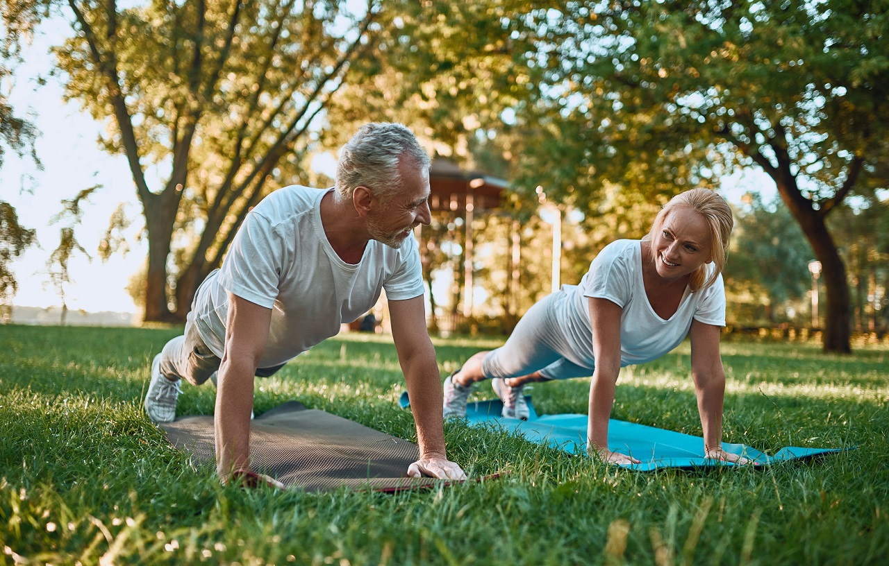 Senior couple is doing sport outdoors. Stretching in park during sunrise
