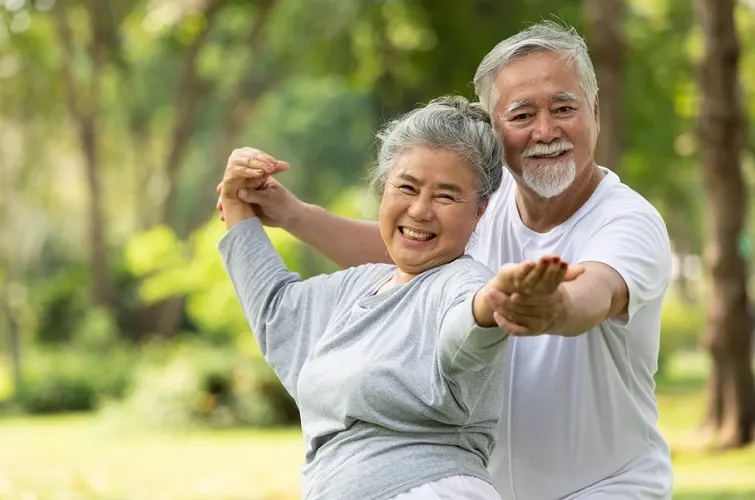 Older man and woman holding hands and practicing yoga in a park